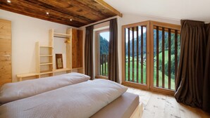 A bedroom with a wooden ceiling, a large window with a view of a green landscape, a bed, and a wooden shelf unit. - Apartment 'Herrischner 1' with Mountain View, Private Terrace and Wi-Fi (Moos in Passeier)