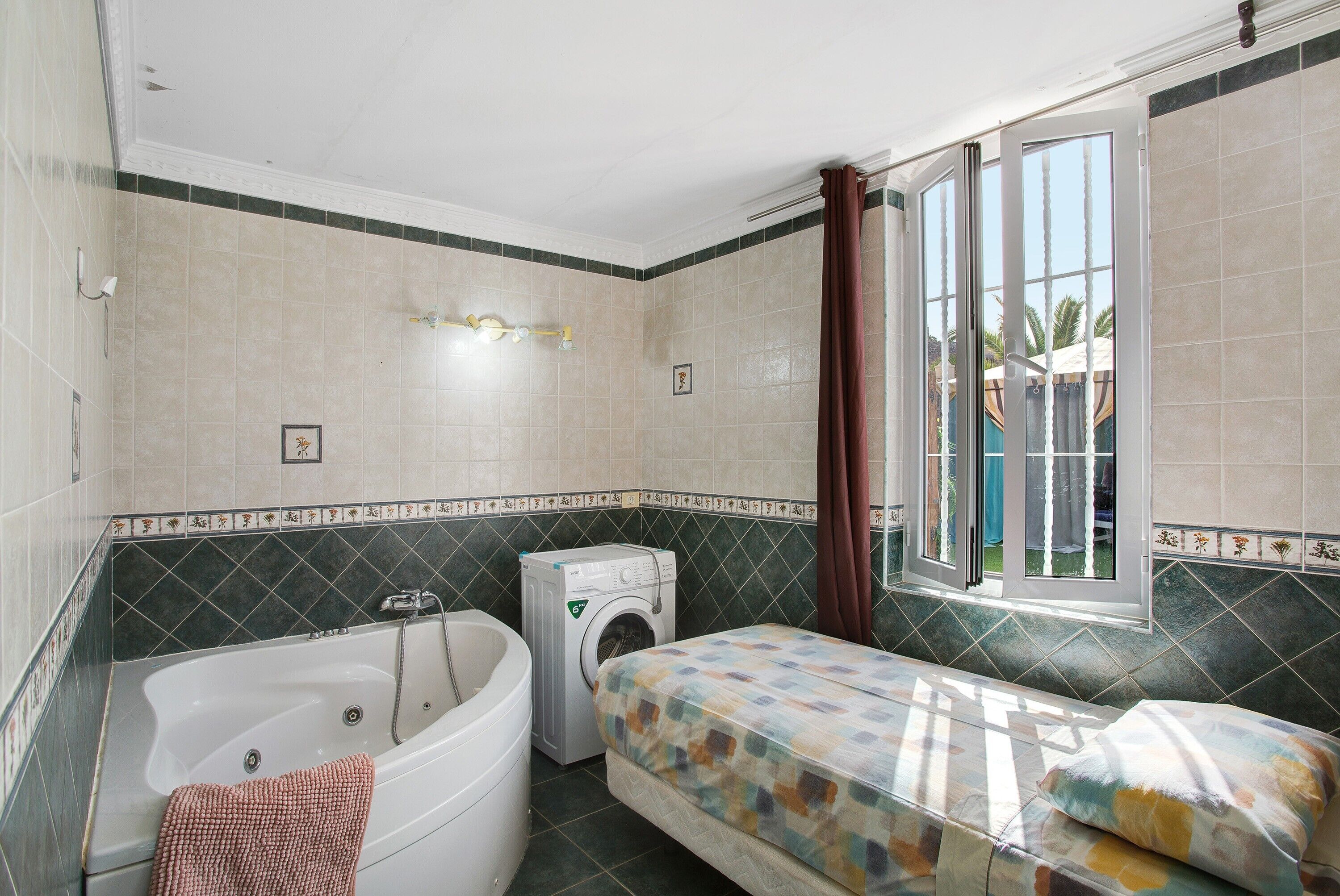 Un baño con bañera, lavadora, cama y ventana con cortinas.