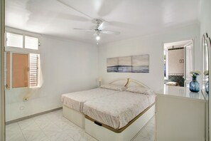A bedroom with a bed, ceiling fan, window with blinds, and a painting on the wall.