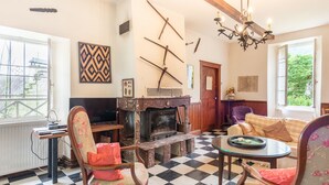 A living room with a fireplace, checkered floor, and a television. - La serre, grande maison  dans un grand jardin. (Laborde)