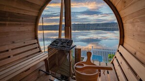 Une cabane en bois dotée d’une fenêtre circulaire qui offre une vue sur un lac et des montagnes.