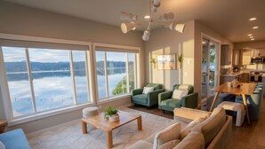 Un salon spacieux avec de grandes fenêtres donnant sur un lac, un coin salon confortable et une cuisine moderne.