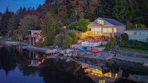 Une propriété située au bord de l’eau, avec une grande maison, des bateaux amarrés et un lac paisible qui reflète le paysage environnant.