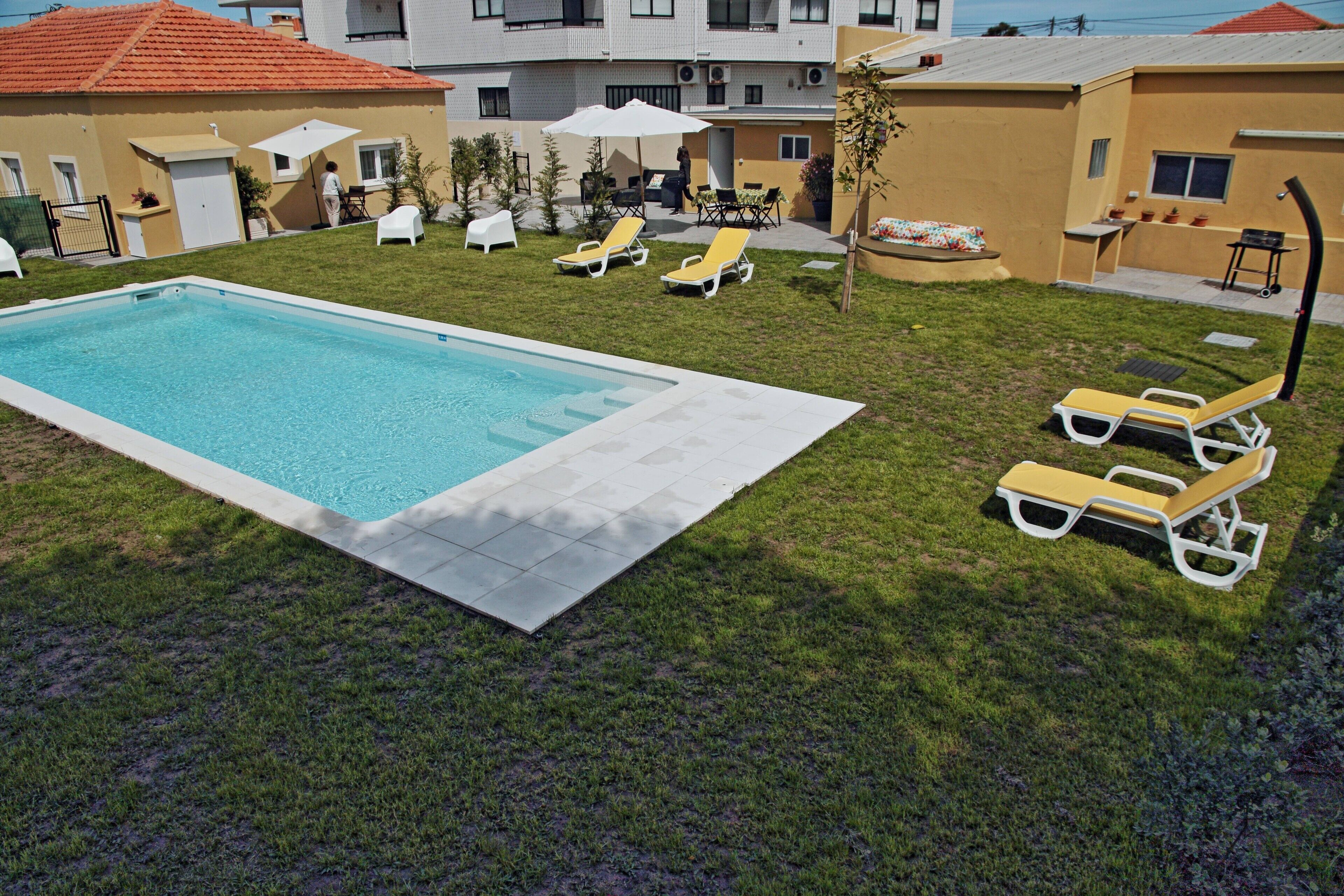 En swimmingpool med liggestole, en lille terrasse og en bygning med rødt tag.