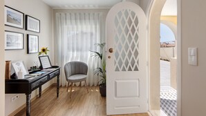 Ein Zimmer mit Schreibtisch, Stuhl, Topfpflanze und einer Tür mit Diamantmuster-Glasscheibe.