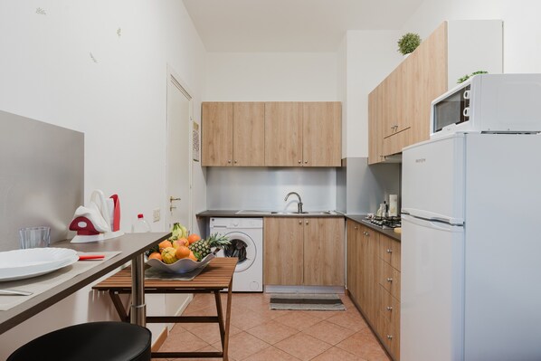 Una cocina funcional con armarios de madera, lavadora, microondas y refrigerador.