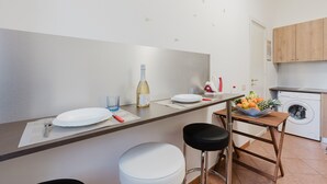 Eine moderne Küche mit Essbereich, einer Waschmaschine und einem kleinen Tisch mit Obst.