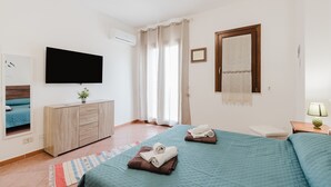Ein Hotelzimmer mit Bett, Fernseher, Nachttisch mit Lampe, Fenster mit Vorhängen und einem Wandspiegel.