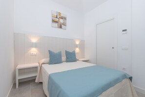 A bedroom with a bed, two bedside tables, a wall-mounted light, a door, and a wall art piece.