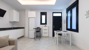 Une cuisine moderne avec des meubles blancs, un plan de travail noir, un coin repas comprenant une table et des chaises blanches, et une porte à cadre noir.