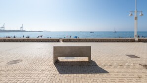 Une promenade en bord de mer, dallée, avec un banc, un muret en pierre et une vue dégagée sur la mer.