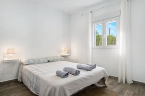 A bedroom with a bed, two bedside lamps, a window with curtains, and a view of greenery outside.