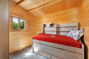 A wooden-paneled room with a bed, a window, and a shelf with books and a decorative item.