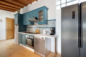 Une cuisine avec des armoires de couleur turquoise, un réfrigérateur en acier inoxydable, un lave-vaisselle et une machine à café.