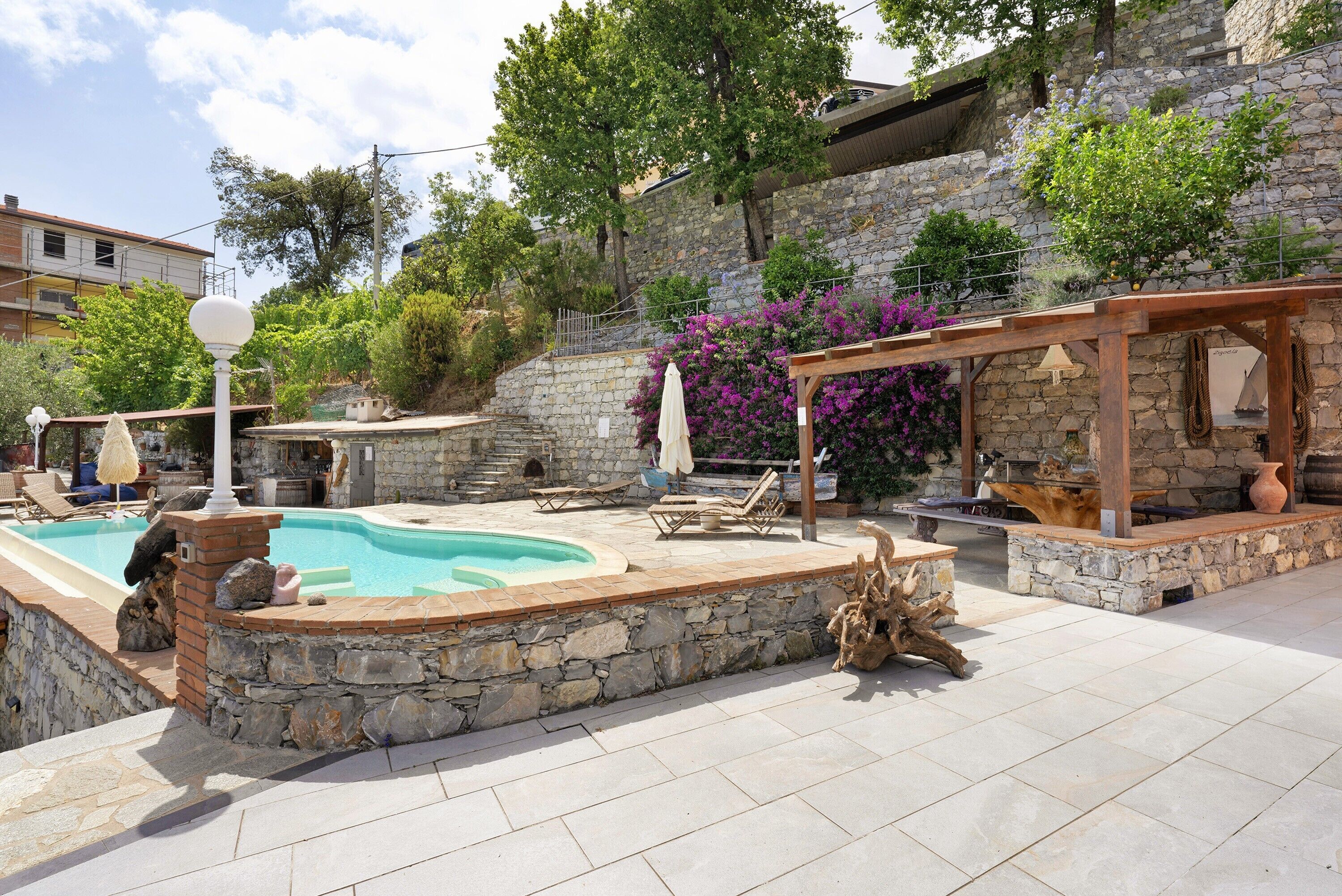 Un área de piscina con muros de piedra, sillas de descanso y una pérgola.