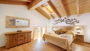 Une chambre avec un plafond en bois, un grand lit, une commode en bois, un miroir et un luminaire fixé au mur.