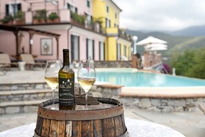 Une bouteille de vin et des verres posés sur un tonneau, près d’une piscine avec vue sur les montagnes.
