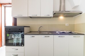A compact kitchen with white cabinets, a stainless steel sink, and a built-in oven.