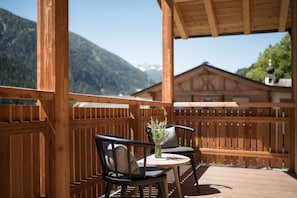 A wooden deck with two chairs and a table, overlooking a mountain.