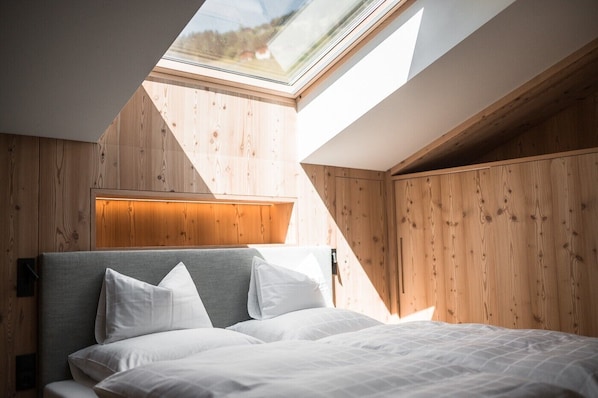 A bedroom with a skylight, wooden walls, and a bed with white bedding.