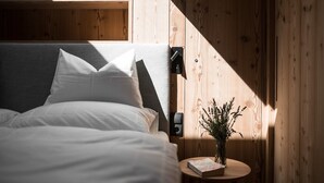 Une chambre à coucher avec un lit, des oreillers, une table de chevet sur laquelle se trouvent un livre et un vase, et des murs en bois.