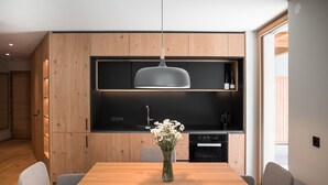 A modern kitchen with wooden cabinets, a black countertop, and a hanging pendant light. - Sunnseit Luxury Apartment 3 – Private Garden & Sauna, Lake View (Ultimo)