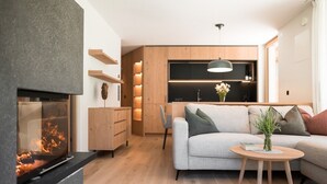 A modern living room with a fireplace, a sofa, a coffee table, and a kitchen area in the background. - Sunnseit Luxury Apartment 3 – Private Garden & Sauna, Lake View (Ultimo)
