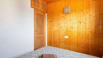A room with wooden walls, a bed with a patterned bedspread, and a wooden door with a mesh screen.