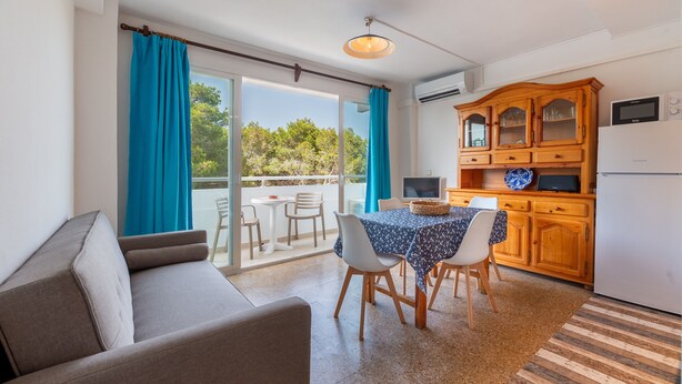 A modern living room with a sofa, dining table, and chairs, a kitchen with wooden cabinets, and a sliding glass door to an outdoor area. - "Pujols 16" Apartment with a Balcony and Air Conditioning (Es Pujols)