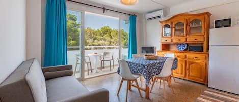 Una sala moderna con sofá, mesa de comedor y sillas, una cocina con armarios de madera y un amplio ventanal corredizo a un espacio exterior.