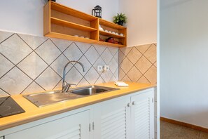 A kitchen with a stainless steel sink, wooden shelves, and a tiled backsplash.