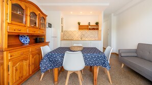 A dining area with a wooden cabinet, a table with chairs, and a kitchen in the background. - "Pujols 16" Apartment with a Balcony and Air Conditioning (Es Pujols)