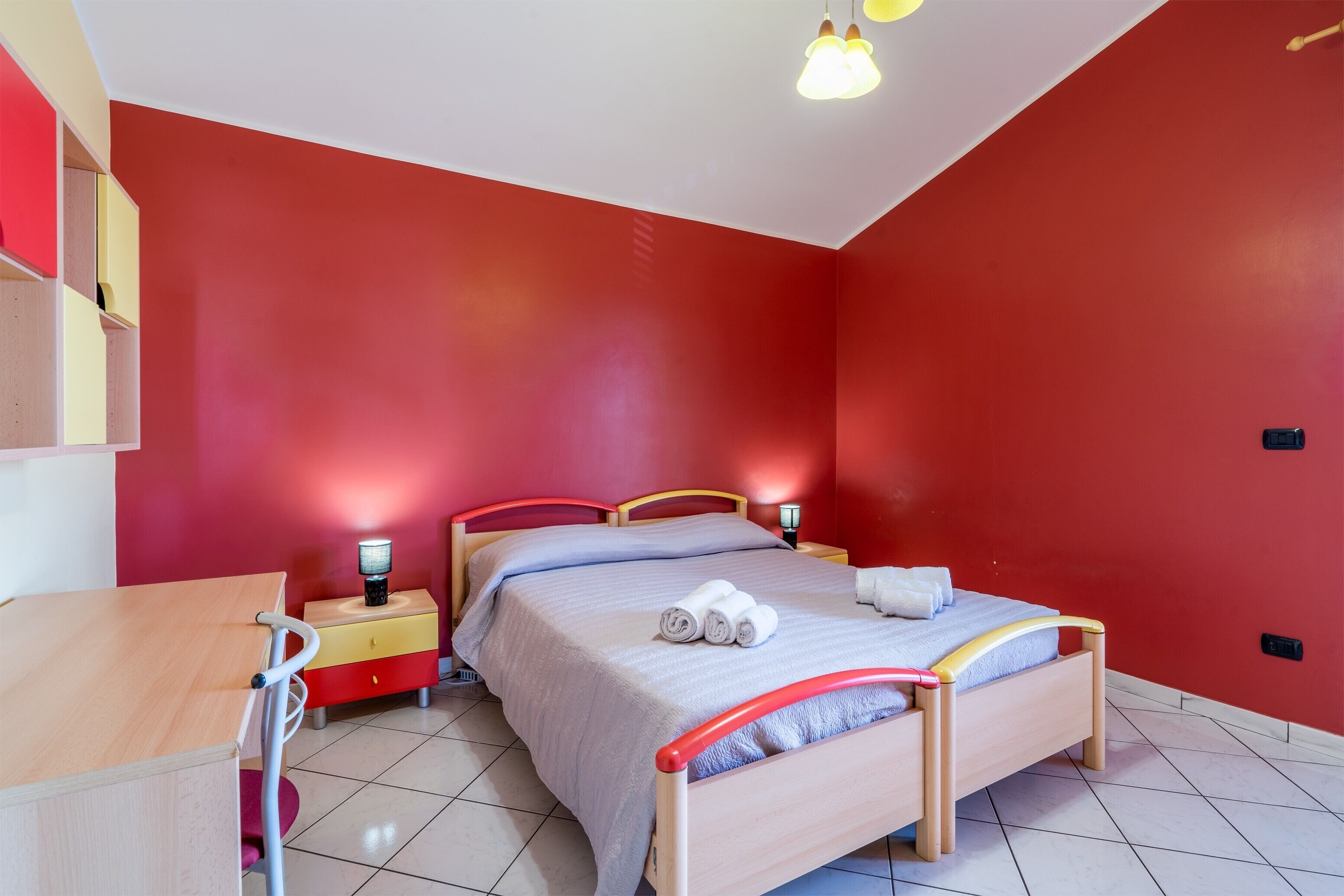 A bedroom with a bed, bedside tables, a desk, and a lamp.