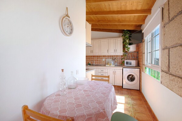 Une cuisine compacte équipée d’un lave-linge, d’un four à micro-ondes et d’un coin repas avec une table et des chaises.