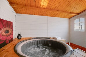 Un bain à remous dans une pièce dotée d’un plafond en bois et de murs blancs, avec une fenêtre et un tableau représentant une fleur rouge.