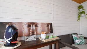 A room with a wooden ceiling, a white wall with horizontal lines, a sofa with a cushion, a small table with a speaker, a tray with cups and a decorative item, and a hanging plant. - Holiday Apartment "Verode" with Sea View, Shared Terrace & Wi-Fi (Arico)