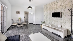 A modern living room with a dining area, a TV mounted on the wall, and a large window. - Holiday Apartment "Los Morales" with Sea View, Shared Terrace & Wi-Fi (Arico)