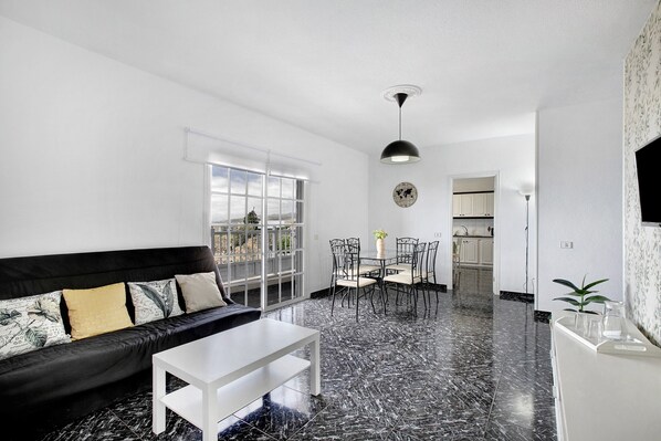 Un salon moderne avec un canapé noir, une table basse blanche et un coin repas comprenant une table et des chaises.