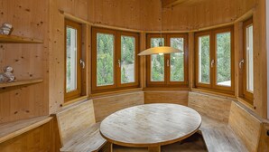 A wooden interior with a round table and benches, large windows with forest views, and a hanging light fixture. - Apartment 'Brugghof Brugg' with Mountain View, Balcony and Wi-Fi (Schnals)