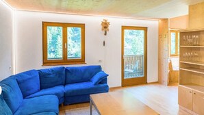 A room with a blue sofa, wooden flooring, a wooden ceiling, two windows with a view of greenery, and a glass door leading outside. - Apartment 'Brugghof Brugg' with Mountain View, Balcony and Wi-Fi (Schnals)