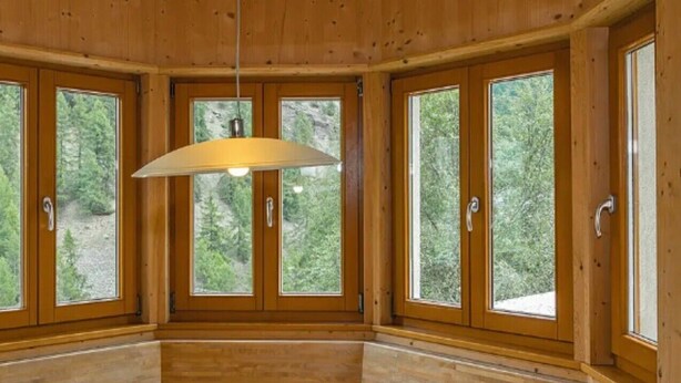 A wooden interior with a round table, large windows, and a hanging light fixture. - Apartment 'Brugghof Brugg' with Mountain View, Balcony and Wi-Fi (Schnals)