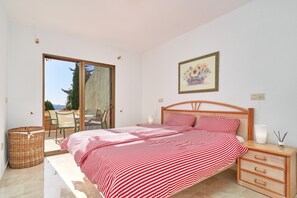 A bedroom with a bed, a nightstand, a wicker basket, a framed picture, and a sliding glass door leading to an outdoor area. - Holiday Apartment "Ombú" with Sea View, Private Terrace & Wi-Fi (La Herradura)