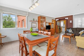 A spacious living area with a dining table, chairs, a sofa, and a television.