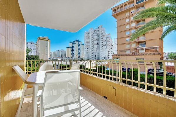 A balcony with a table and chairs, a view of high-rise buildings, and a railing.