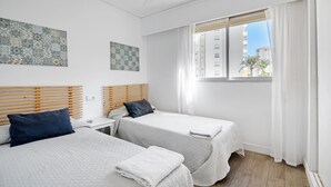 A hotel room with two beds, a ceiling fan, a window with curtains, and artwork on the walls. - Apartment 'Roma' with Shared Pool, Wi-Fi and Air Conditioning (Platja de Gandia)