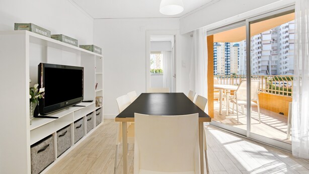 A modern living room with a flat-screen TV, white furniture, and a balcony with a view of high-rise buildings. - Apartment 'Roma' with Shared Pool, Wi-Fi and Air Conditioning (Platja de Gandia)