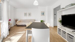 A modern living room with a dining table, white furniture, a flat-screen TV, and artwork on the walls. - Apartment 'Roma' with Shared Pool, Wi-Fi and Air Conditioning (Platja de Gandia)