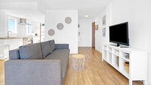 A modern living room with a grey sofa, a TV on a white stand, and a round wooden side table. - Apartment 'Playa Puig' with Shared Pool, Wi-Fi and Air Conditioning (El Puig de Santa Maria)