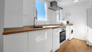 A modern kitchen with white cabinetry, a wooden countertop, a built-in oven, a microwave, and a washing machine. - Apartment 'Playa Puig' with Shared Pool, Wi-Fi and Air Conditioning (El Puig de Santa Maria)