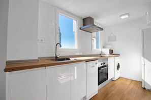 Een moderne keuken met witte kasten, een houten aanrecht, een ingebouwde oven, een magnetron en een wasmachine.